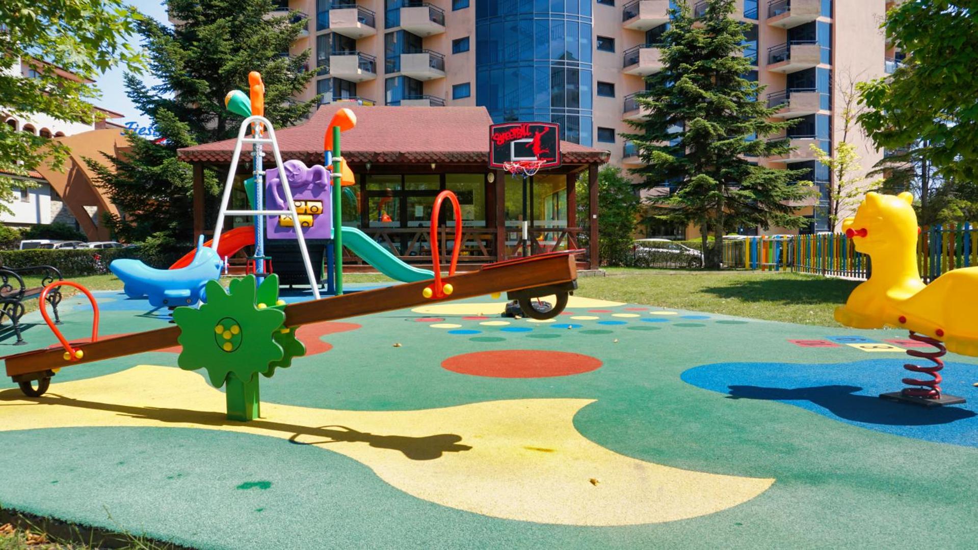 DIT Majestic Beach Resort bērnu atpūtas zona ar šūpolēm un basketbola grozu uz mīkstā seguma pie viesnīcas korpusa