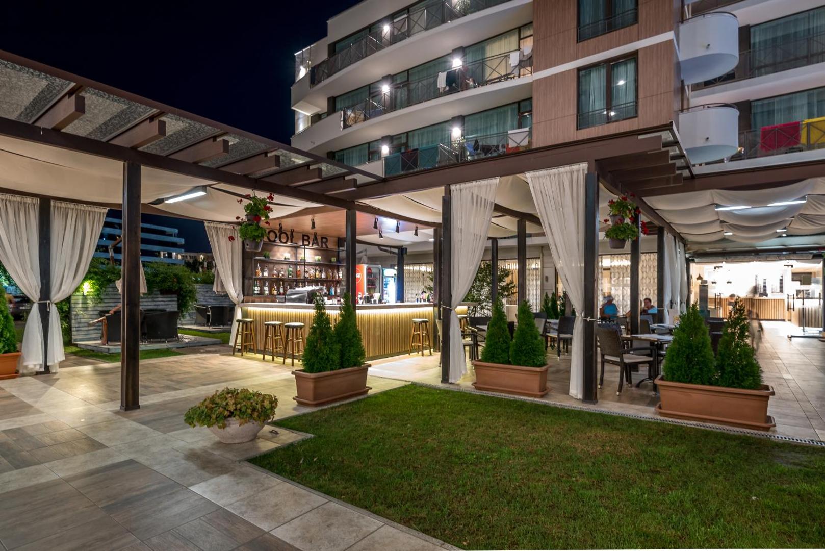 Lion Sunny Beach Hotel āra bārs vakarā ar apgaismotu leti, sēdvietām zem nojumes un skatu uz viesnīcas fasādi