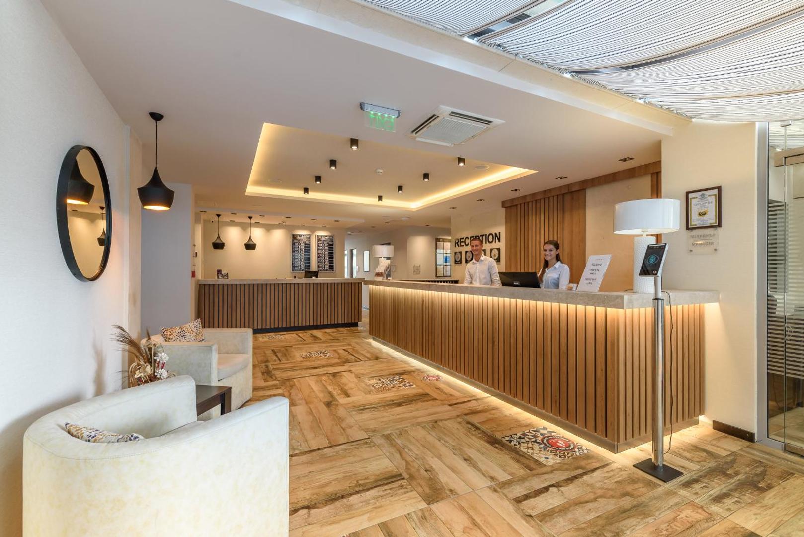 Lion Sunny Beach Hotel moderna recepcijas zona ar koka apdari, gaišu interjeru un viesmīlīgu personālu kūrortā Saulainais krasts