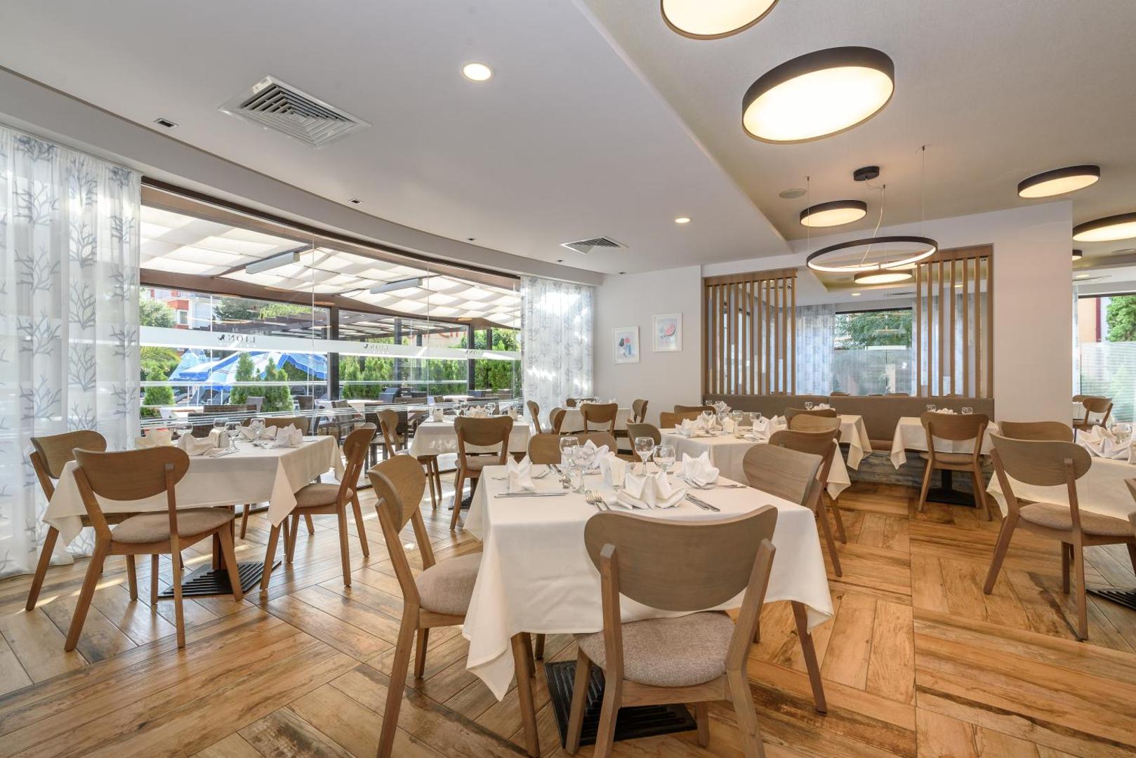 Lion Sunny Beach Hotel restorāna zāle ar klātiem galdiem, koka grīdu un modernu apgaismojumu gaišos toņos