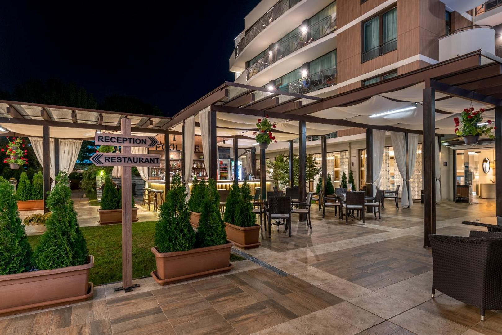 Lion Sunny Beach Hotel terase ar norādēm uz restorānu un baseinu, mīkstajām mēbelēm un dekoratīviem augiem vakarā