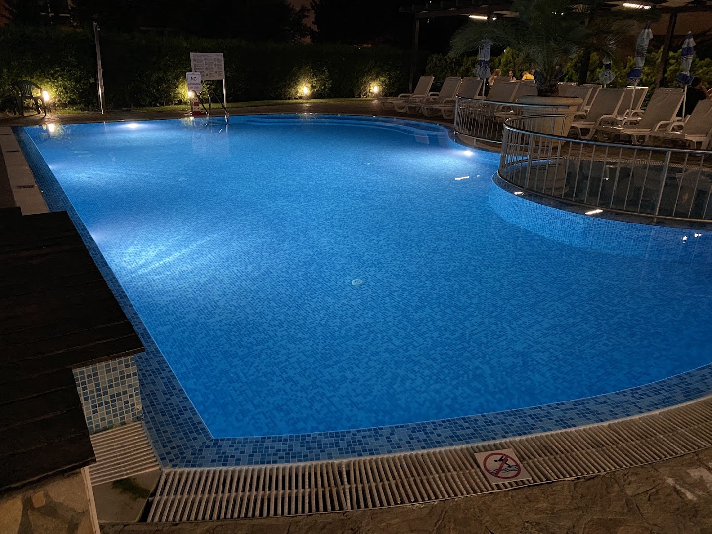 Lion Sunny Beach Hotel baseina nakts apgaismojums, zilas flīzes un sauļošanās krēsli fonā Saulainajā krastā