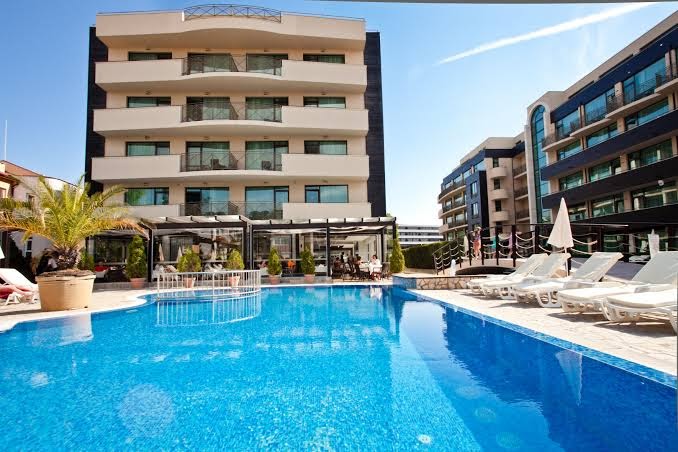 Lion Sunny Beach Hotel galvenā ēka ar balkoniem un plašu āra baseinu, sauļošanās krēsli un saulessargi Saulainajā krastā