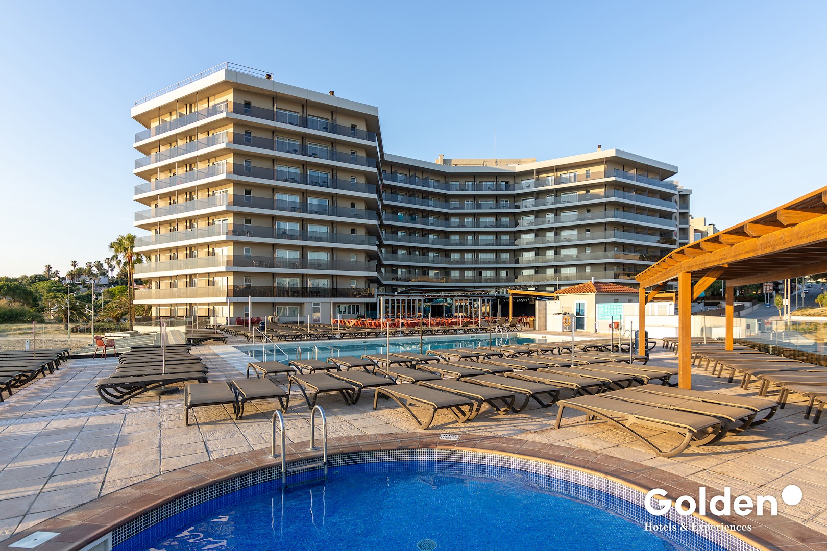 Golden Donaire Beach viesnīcas ēka un āra baseins ar sauļošanās krēsliem Kostadoradas piekrastē, Spānijā — skats no baseina malas