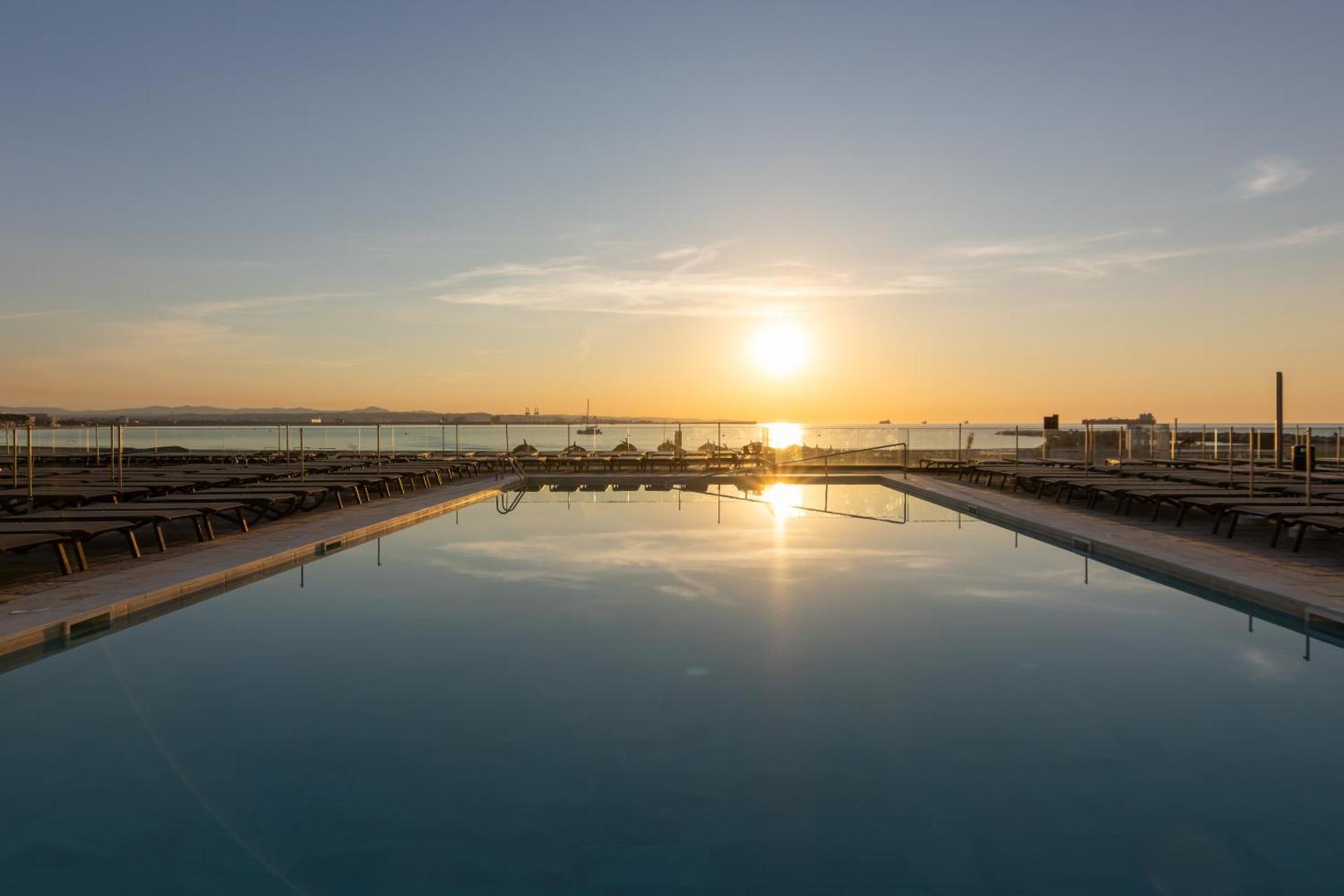 Saulriets virs Vidusjūras, skatoties no Golden Donaire Beach viesnīcas baseina terases ar stikla nožogojumu