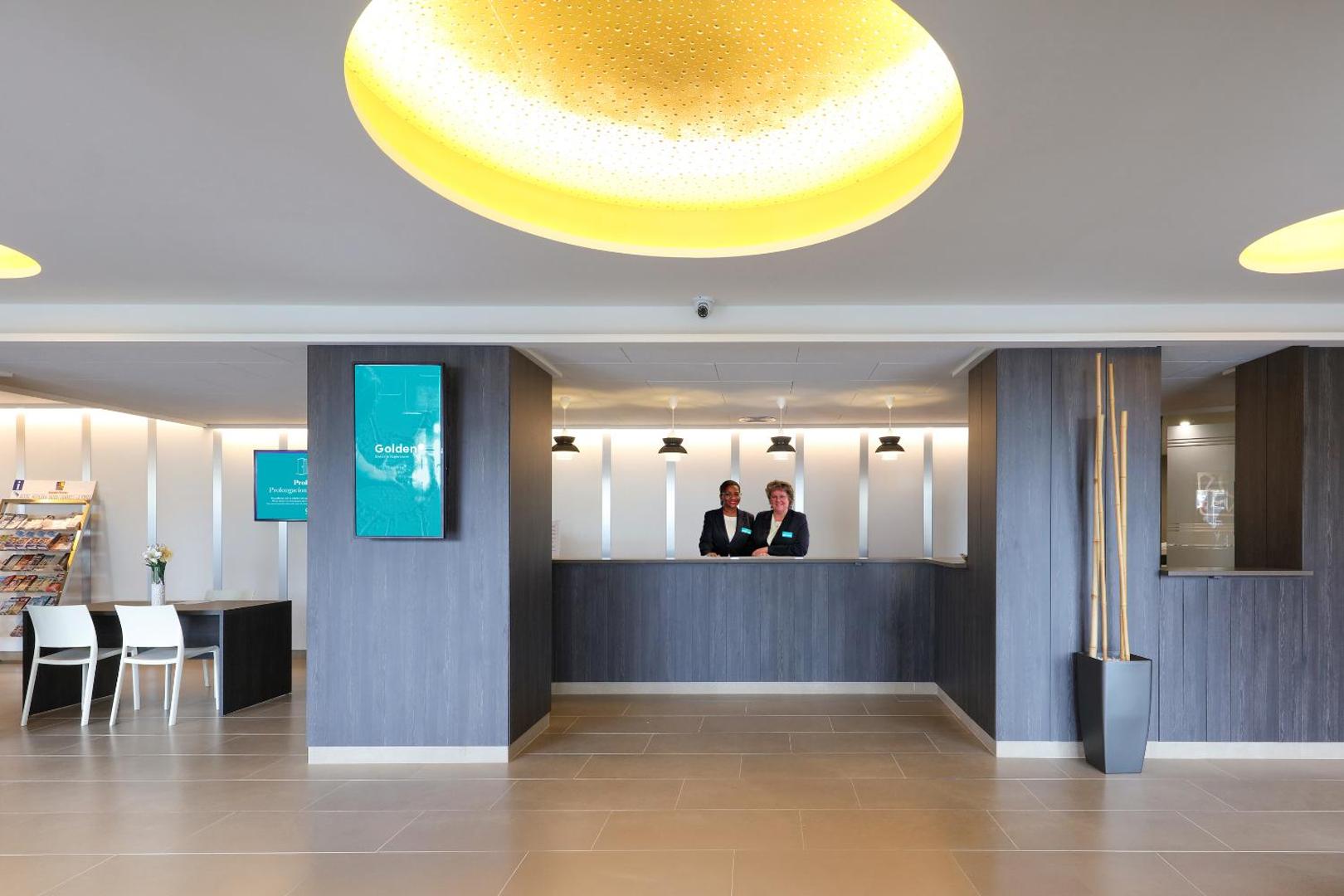Golden Donaire Beach viesnīcas modernā recepcija ar personālu, tumša koka apdari un stilīgiem gaismas ķermeņiem vestibilā