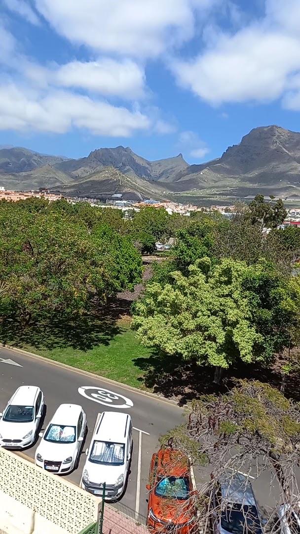 Skats no Best Jacaranda viesnīcas Tenerifē uz kalnu grēdu, zaļojošu parku un stāvvietu ar automašīnām saulainā dienā.