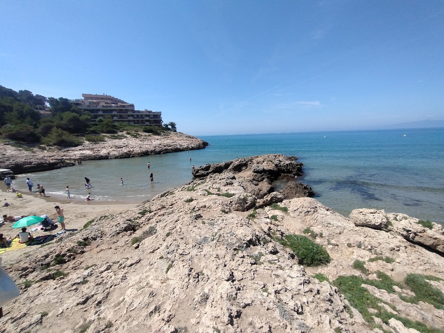 Hotel Cala Font skats uz klinšainu līci un smilšu pludmali Salovā, Spānijā — tirkīzzils ūdens un atpūtnieki piekrastē