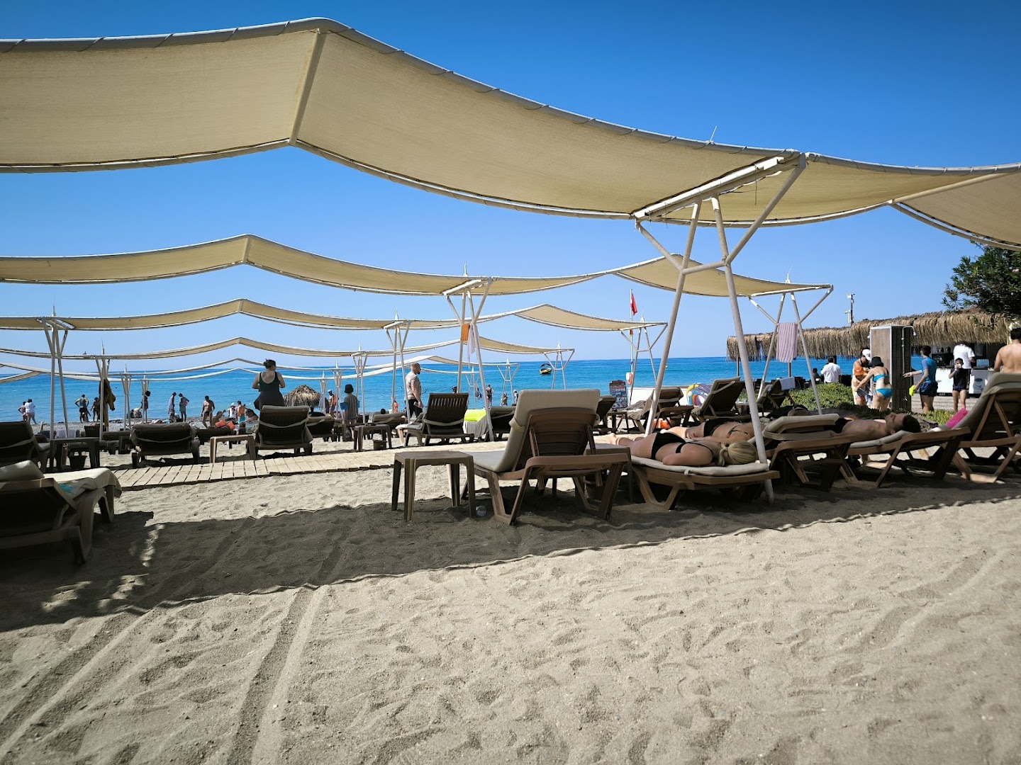 Atpūtnieki zem lielām saules nojumēm The Garden Beach Hotel pludmales zonā pie jūras