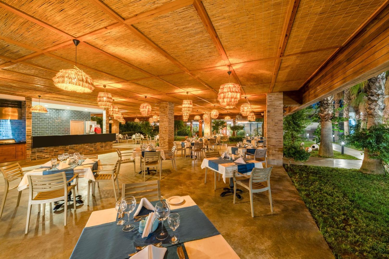 The Garden Beach Hotel dārza restorāns vakarā ar pītiem gaismekļiem un skatu uz palmu dārzu Turcijā