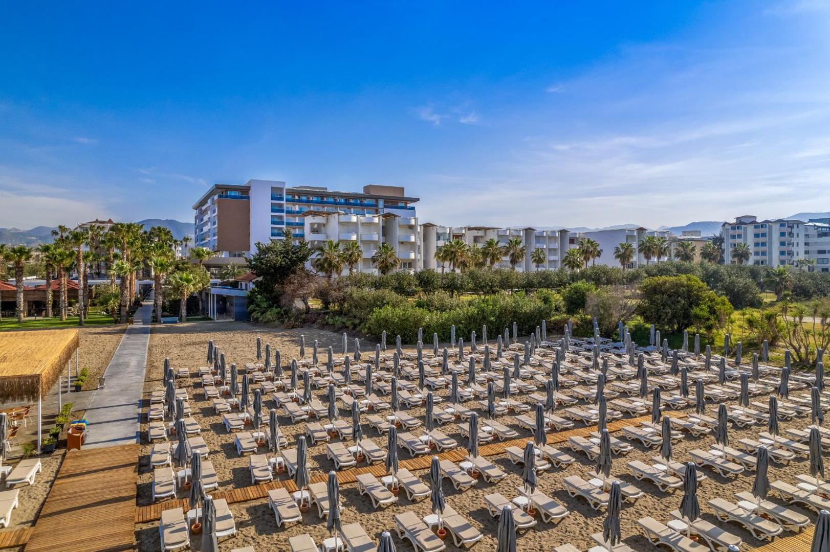 The Garden Beach Hotel skats no augšas uz plašo smilšu pludmali ar saulessargiem un viesnīcas ēku fonā Konakli reģionā