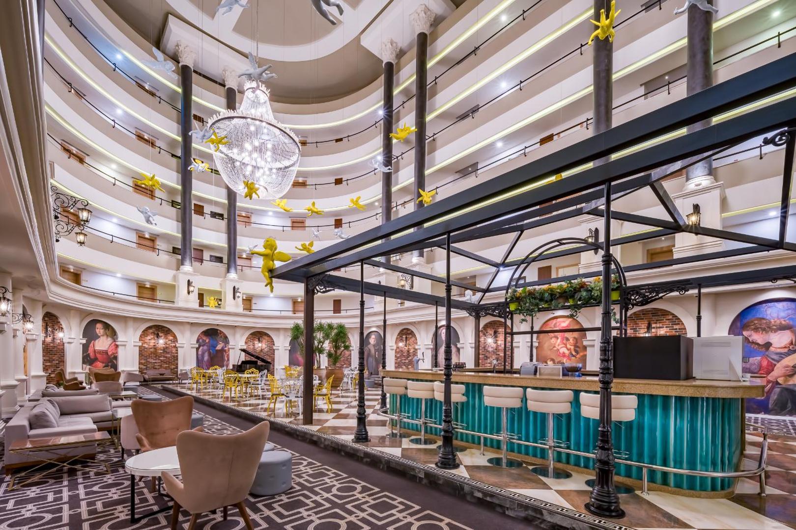The Garden Beach Hotel iespaidīgais ātrijs ar vairākiem stāviem, bāru centrā, klasiskām gleznām un dekoratīviem eņģeļiem