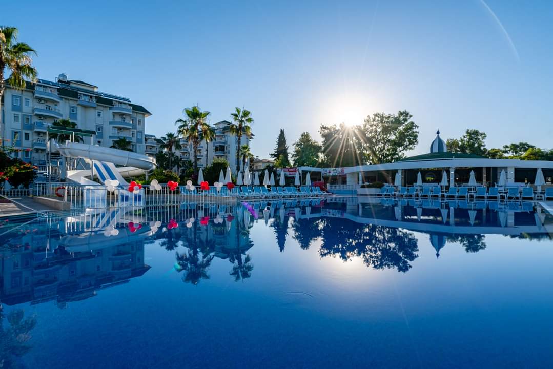 The Garden Beach Hotel baseins saulrietā ar ēku atspulgu ūdenī — Alanjas piekrastes kūrorta vakara atmosfēra