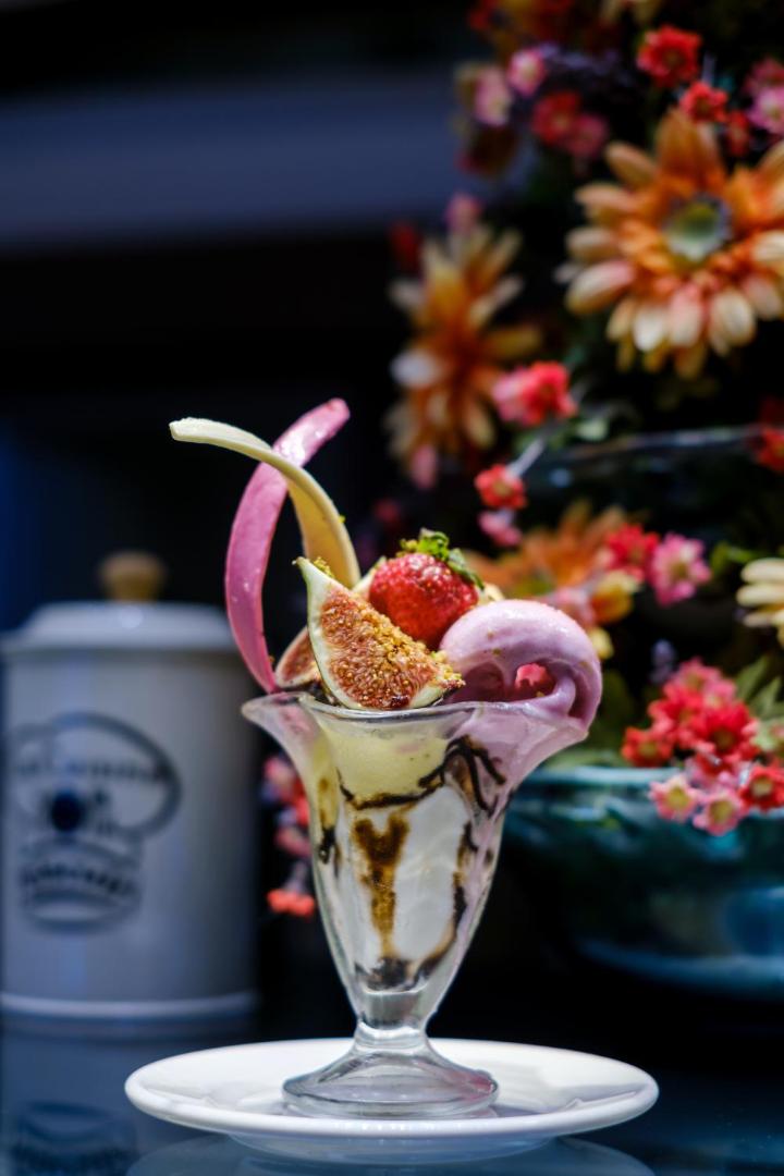 Saldējuma deserts ar svaigām vīģēm un zemenēm The Garden Beach Hotel restorānā uz ziedu fona