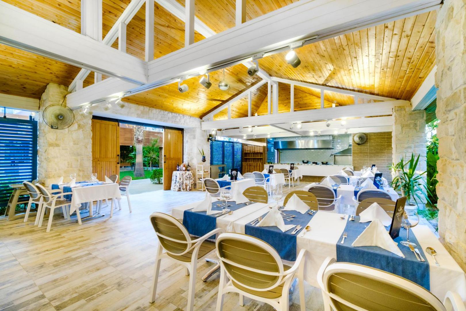 The Garden Beach Hotel a la carte restorāns ar gaišu koka interjeru un elegantiem galda klājumiem Alānijā