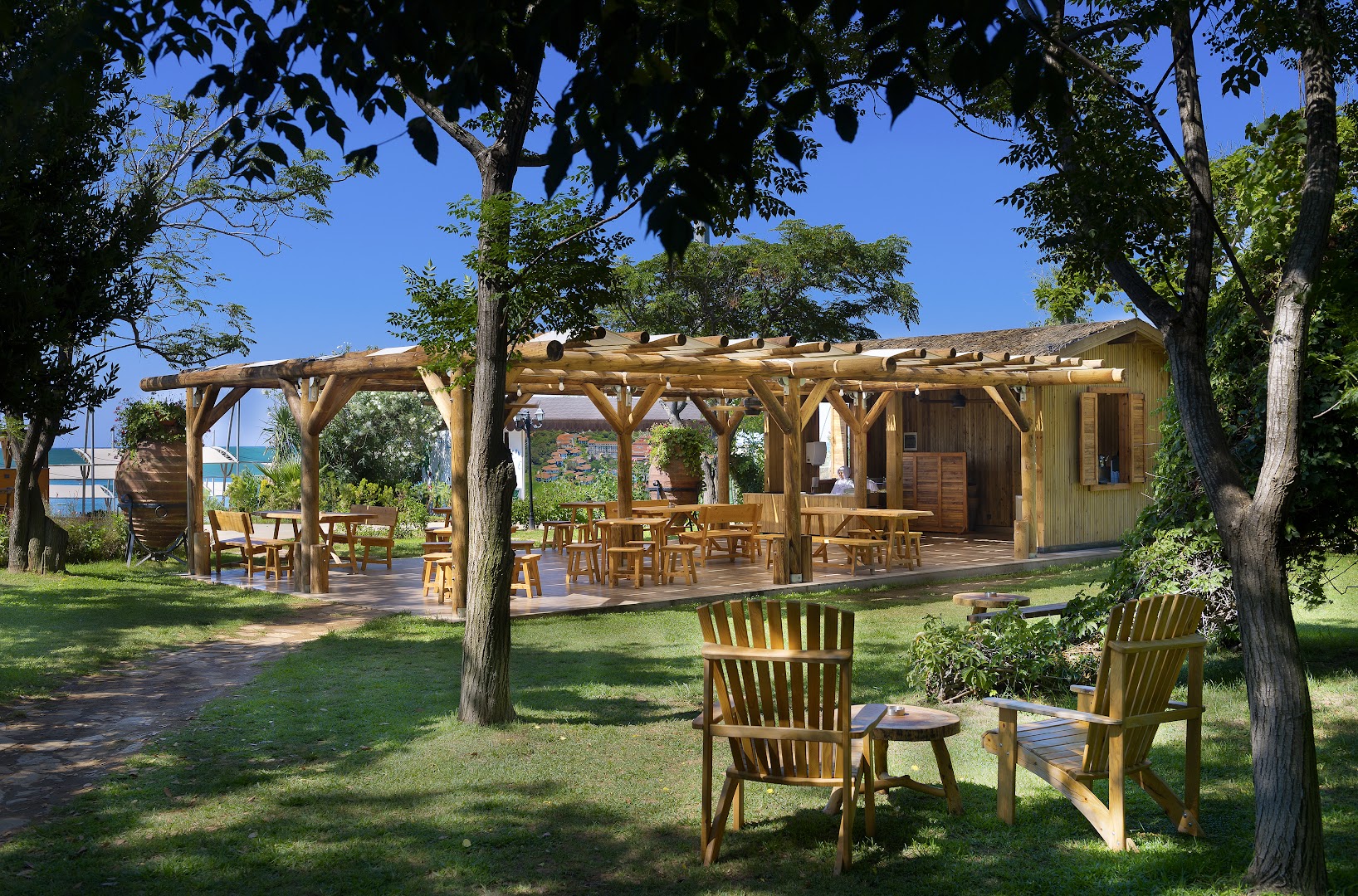 Belconti Resort Hotel dārza bārs ar koka konstrukcijām Belekā — atpūtas zona ar koka krēsliem un galdiem zaļā zālājā koku pavēnī