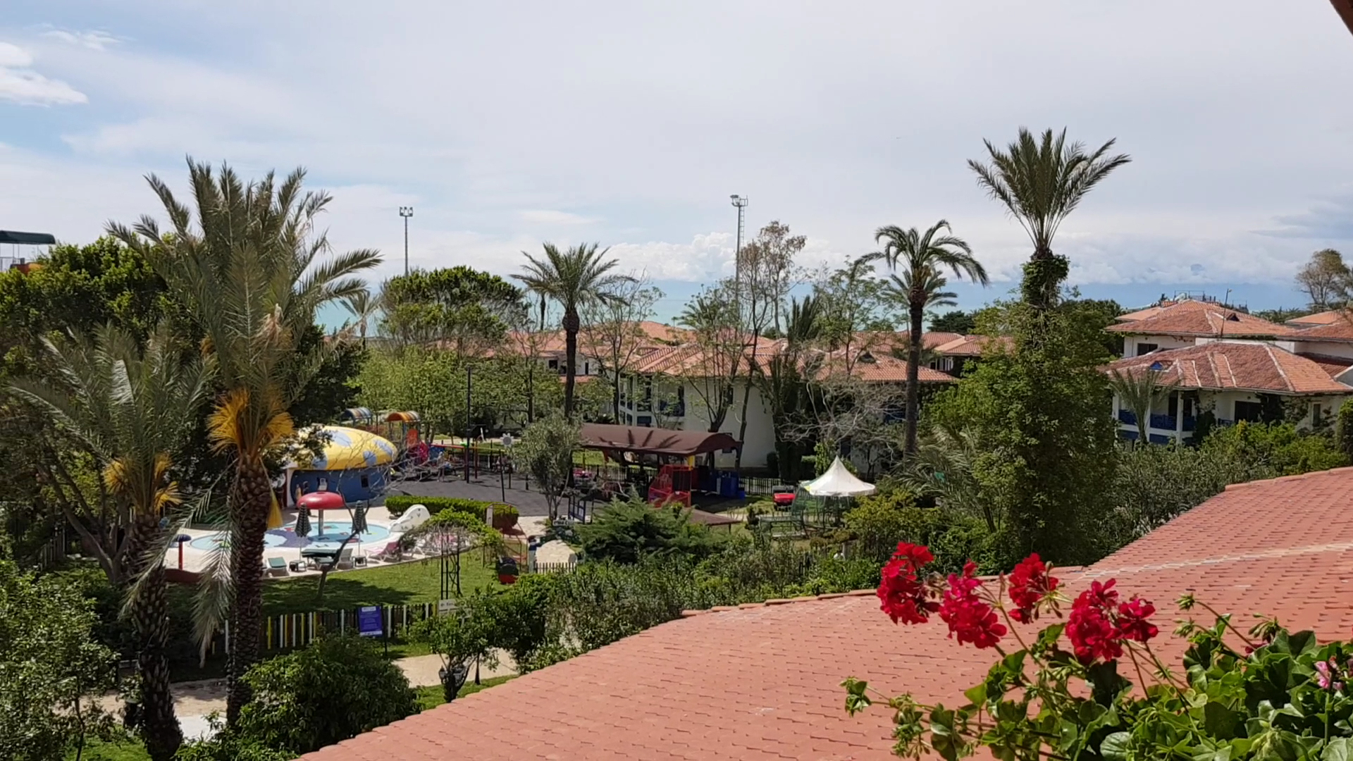 Skats no Belconti Resort Hotel terases uz zaļo teritoriju, bērnu rotaļu laukumu un bungalo tipa ēkām dārza ieskāvumā