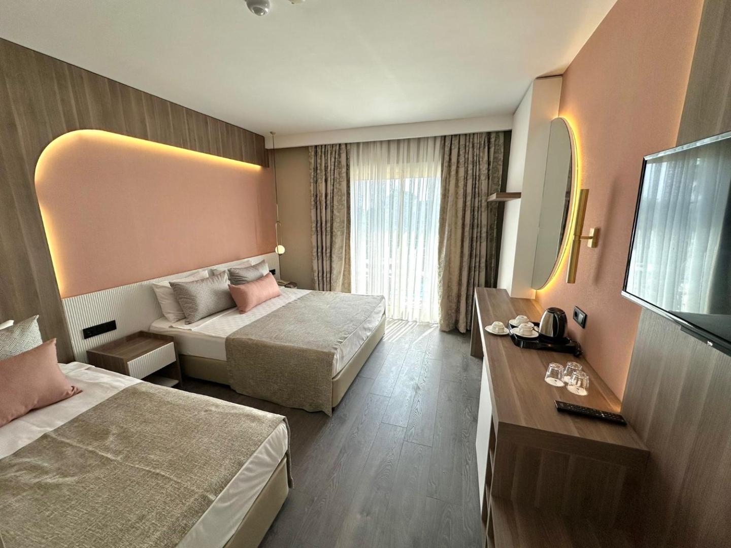 L'oceanica Beach Resort Hotel numurs ar divām gultām, rozā sienas paneli un apaļu spoguli — silts apgaismojums un mūsdienīgs iekārtojums