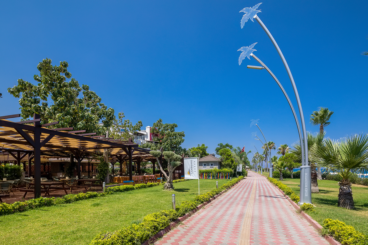 L'oceanica Beach Resort Hotel labiekārtota gājēju promenāde ar palmām, dekoratīviem apgaismes stabiem un āra terasi kreisajā pusē