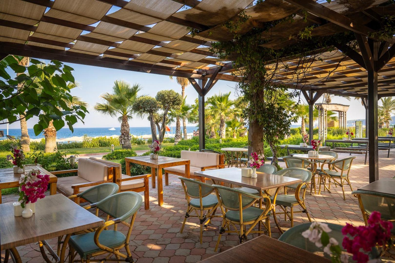 L'oceanica Beach Resort Hotel āra terases restorāns ar skatu uz jūru un palmām Kemeras reģionā, Turcijā — koka mēbeles un ziedu dekori