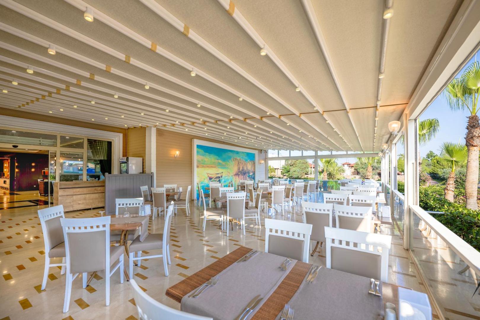 L'oceanica Beach Resort Hotel segtā āra terase ar baltām mēbelēm un skatu uz dārzu — gaiša atpūtas zona ar nojumi
