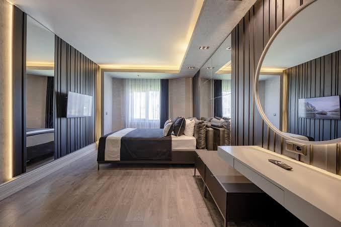 L'oceanica Beach Resort Hotel luksusa numurs ar tumša koka paneļiem, lielu spoguli un iebūvētu apgaismojumu — elegants un moderns interjers