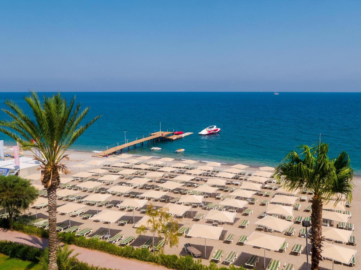 Skats no augšas uz L'oceanica Beach Resort Hotel pludmali, koka piestātni un palmu ieskautu atpūtas zonu Kemerā
