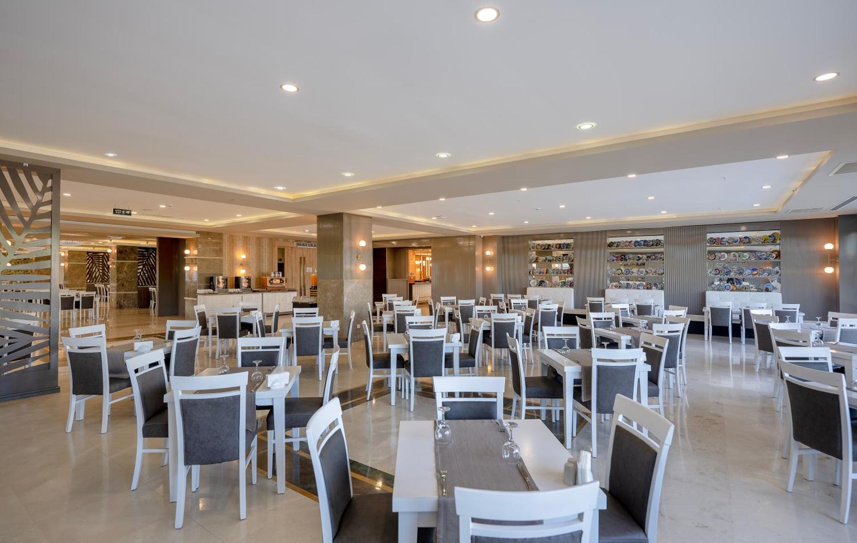 L'oceanica Beach Resort Hotel galvenais restorāns ar gaišu interjeru, baltiem galdiem un pelēkiem krēsliem — plaša un moderna ēdamzāle