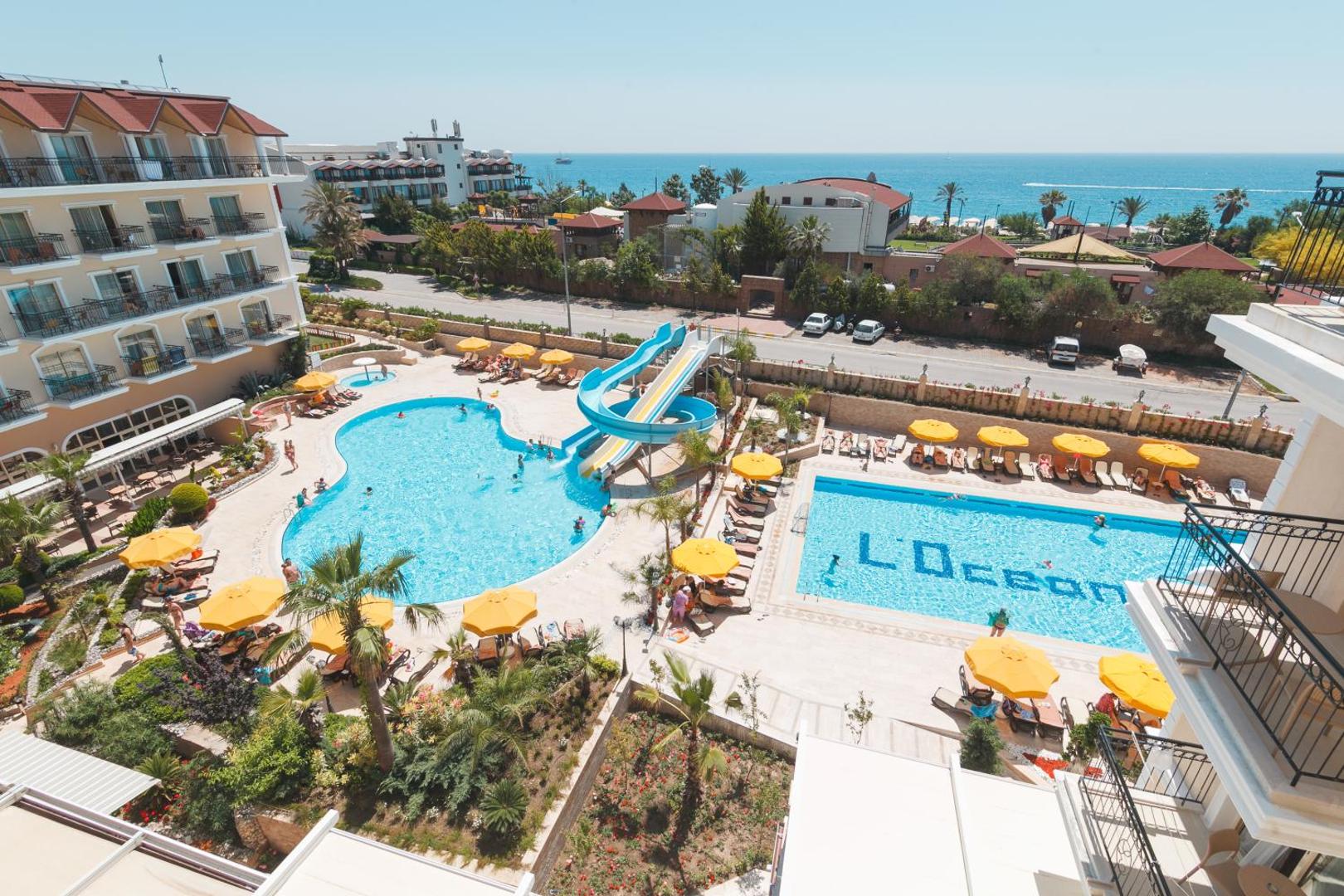 Panorāmas skats no L'oceanica Beach Resort Hotel uz baseiniem, dārzu un Vidusjūras piekrasti tālumā Kemeras apkārtnē.
