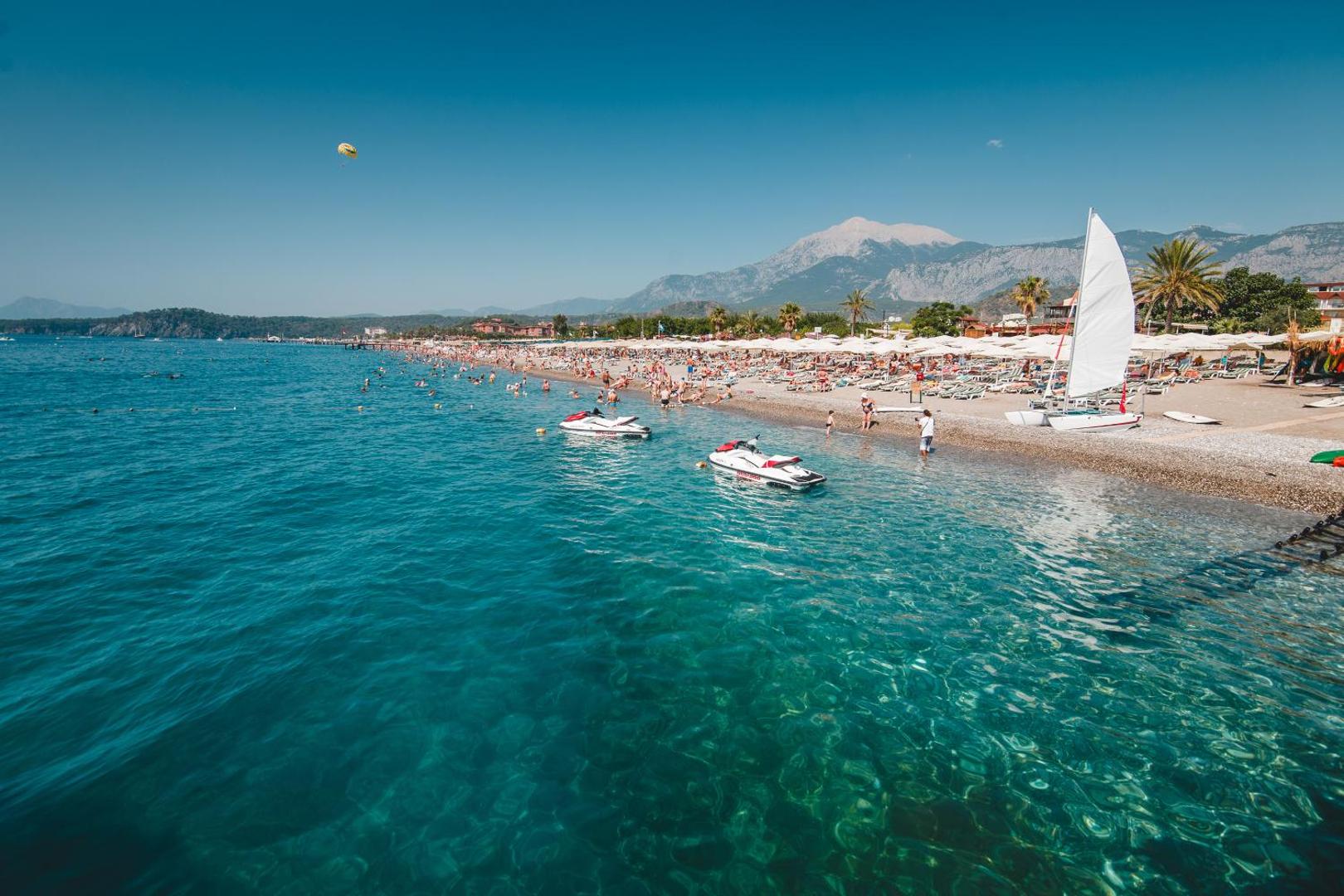 L'oceanica Beach Resort Hotel oļu pludmale Čamjuvā, Kemerā — dzidrs tirkīza ūdens, ūdensmotocikli un skats uz kalniem tālumā