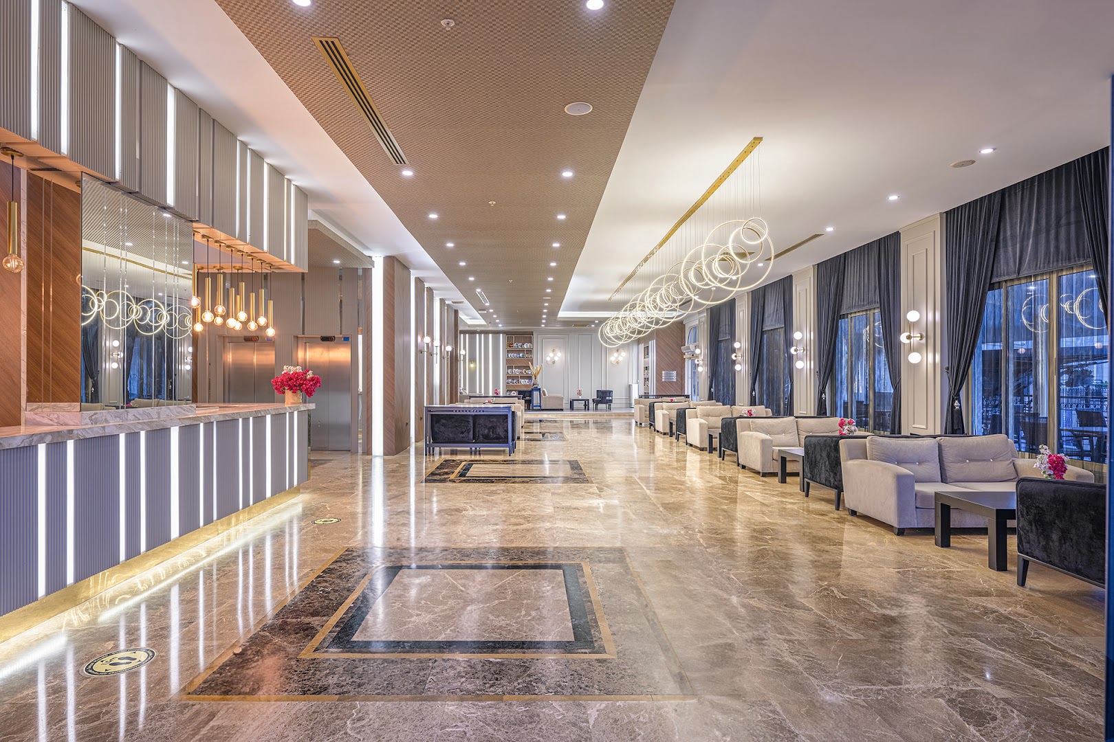 L'oceanica Beach Resort Hotel recepcijas zona ar gaišu marmora apdari, modernām lustrām un ērtām sēdvietām viesu uzņemšanai