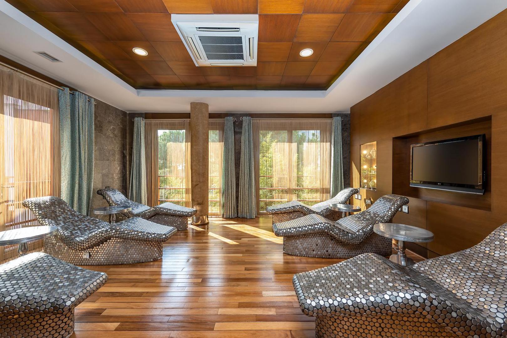 Cornelia Diamond Golf Resort & Spa relaksācijas telpa ar ergonomiskiem zviļņiem, koka apdari un skatu uz priežu mežu Belekā