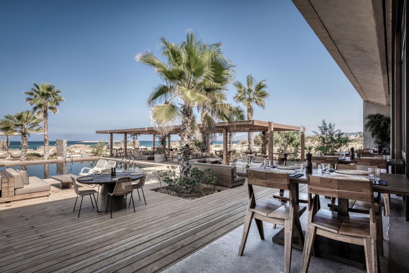 Domes Zeen Chania ēdienkartes restorāns ar koka mēbelēm un terasi pie baseina ar skatu uz jūru un palmām
