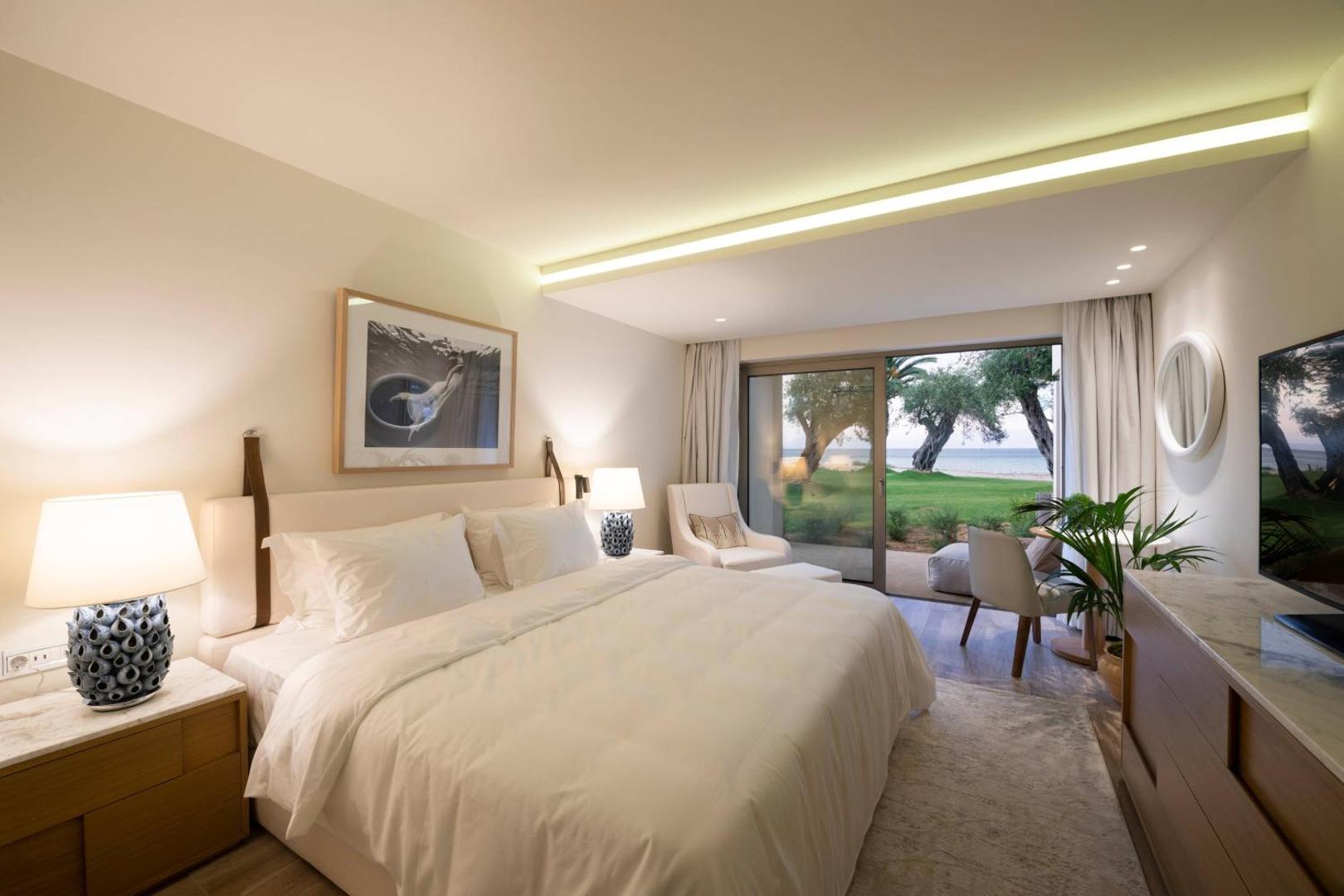 Domes Miramare Resort gaišs numurs ar skatu uz dārzu un jūru Korfu salā — liela gulta, atpūtas krēsls un terase