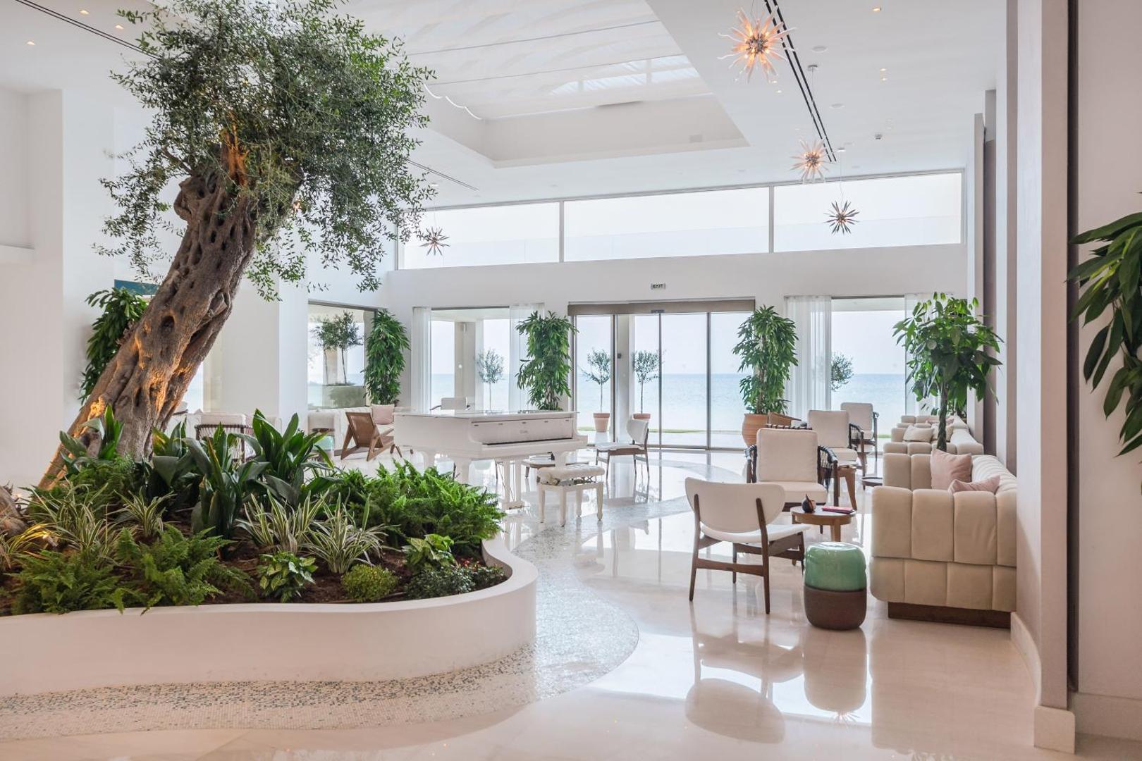 Domes Miramare Resort lobby halle ar baltu flīģeli, olīvkoku un gaišām mēbelēm — plašs interjers ar skatu uz jūru