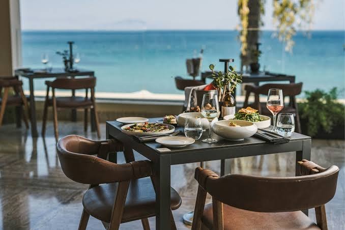 Domes Miramare Resort restorāna galda klājums ar Vidusjūras virtuves ēdieniem un vīna glāzēm uz jūras fona Korfu
