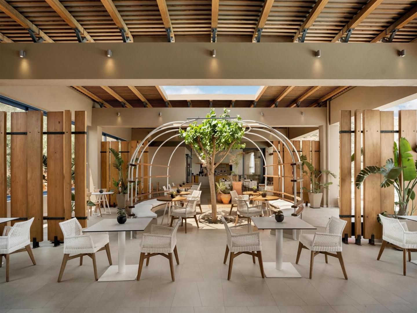 Domes Aulus Elounda Resort restorāna terase ar modernām mēbelēm, koka apdari un dzīvu koku centrā Elundā, Krētā