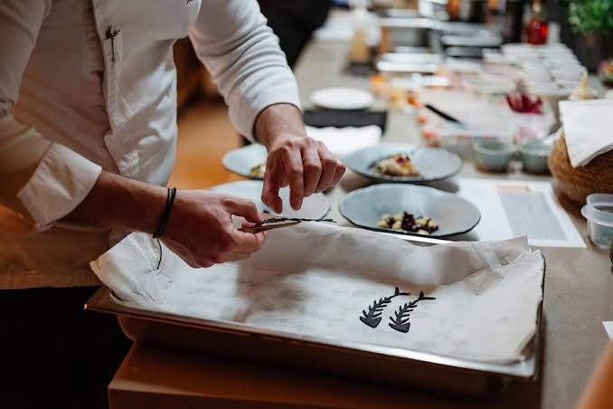 Domes Noruz Chania šefpavārs gatavo izsmalcinātu ēdienu, izmantojot dekoratīvus elementus — augstas klases gastronomija viesnīcas virtuvē