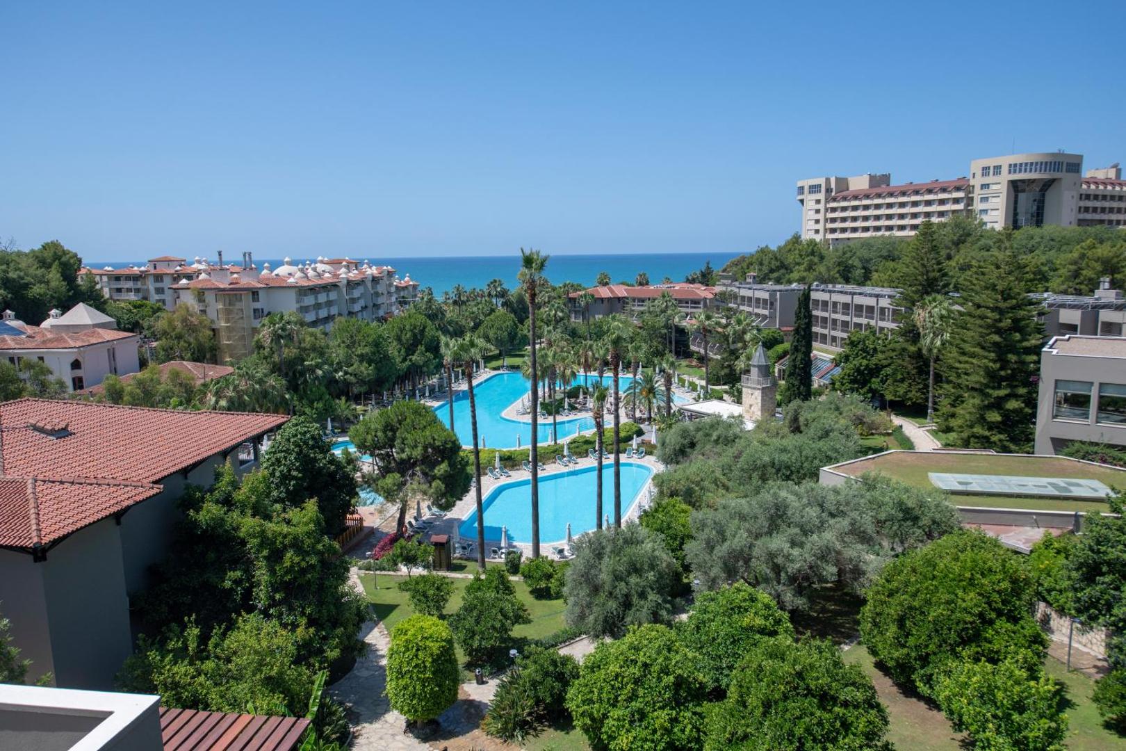 Panorāmas skats no Barut Hemera viesnīcas uz baseiniem, zaļo dārzu un jūras piekrasti tālumā