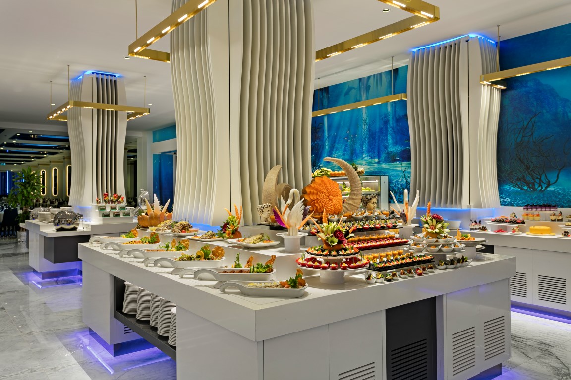 Limak Atlantis De Luxe restorāna bufetes galds ar mākslinieciski noformētām uzkodām un desertiem uz balta marmora virsmām