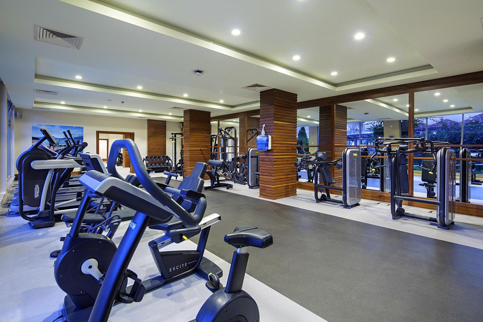 Bellis Deluxe Hotel moderns fitness centrs ar Technogym trenažieriem, koka apdari un plašiem spoguļiem Belekā