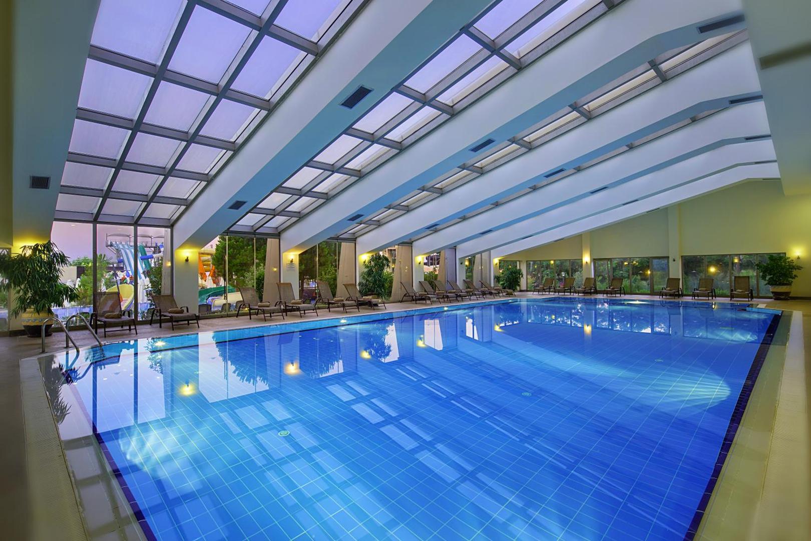 Bellis Deluxe Hotel iekštelpu baseins ar stikla jumtu un atpūtas krēsliem — gaiša un moderna spa zona