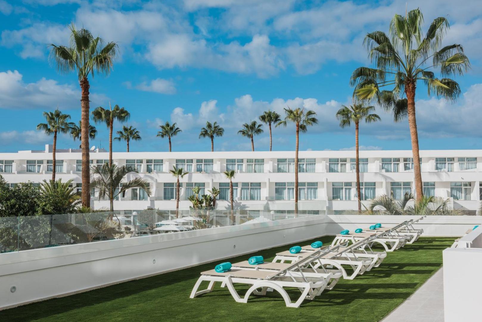 Iberostar Waves Las Dalias sauļošanās terase ar moderniem zviļņiem un palmām uz zila debess fona Tenerifes kūrortā