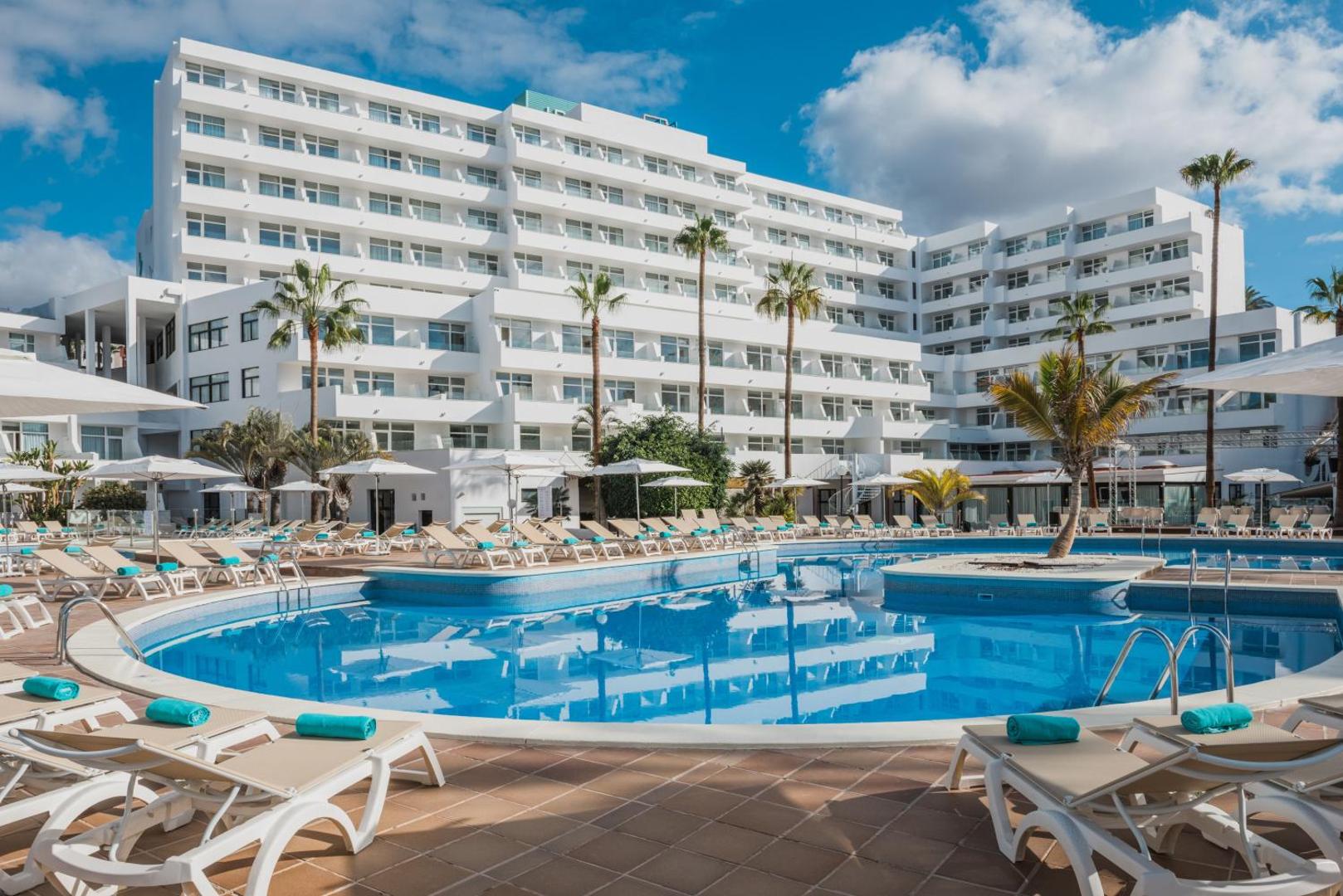 Iberostar Waves Las Dalias viesnīcas fasāde un lielais āra baseins Tenerifē — sauļošanās krēsli, saulessargi un palmas pie baseina