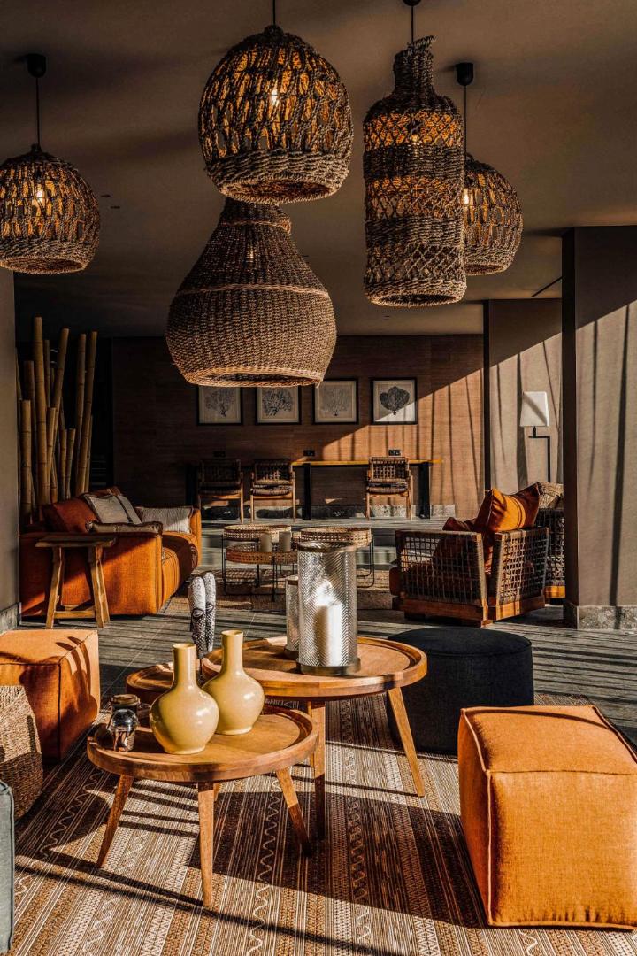 Cook's Club Corfu viesnīcas atpūtas zona ar pītiem gaismekļiem, koka galdiņiem un siltas krāsas mīkstajām mēbelēm boho stilā