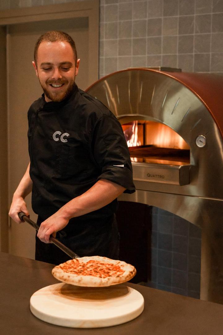 Cook's Club Corfu pavārs pie tradicionālās picu krāsns gatavo svaigu picu viesnīcas restorānā Grieķijā