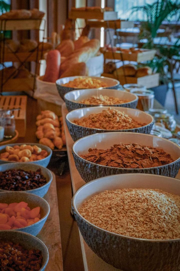Brokastu bufete Cook's Club Corfu viesnīcā ar plašu pārslu, sēklu, žāvētu augļu un svaigas maizes izvēli keramikas traukos