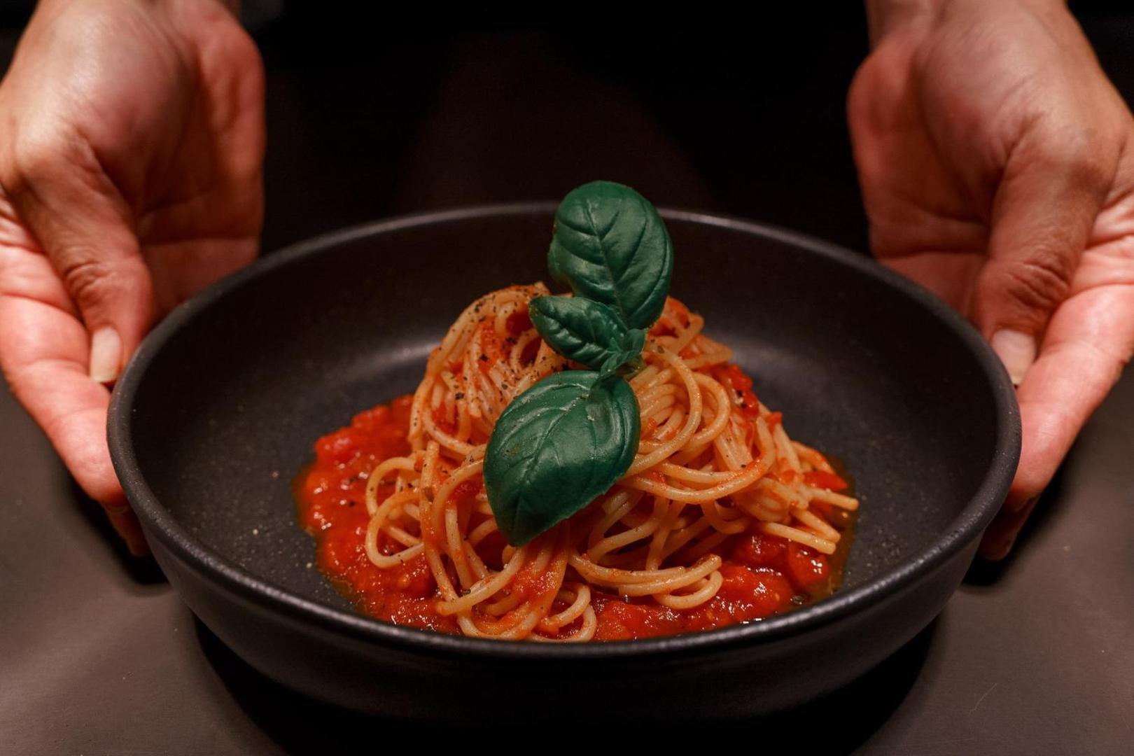 Cook's Club Corfu restorāna ēdiens — klasiska pasta ar tomātu mērci un svaigu baziliku melnā keramikas traukā