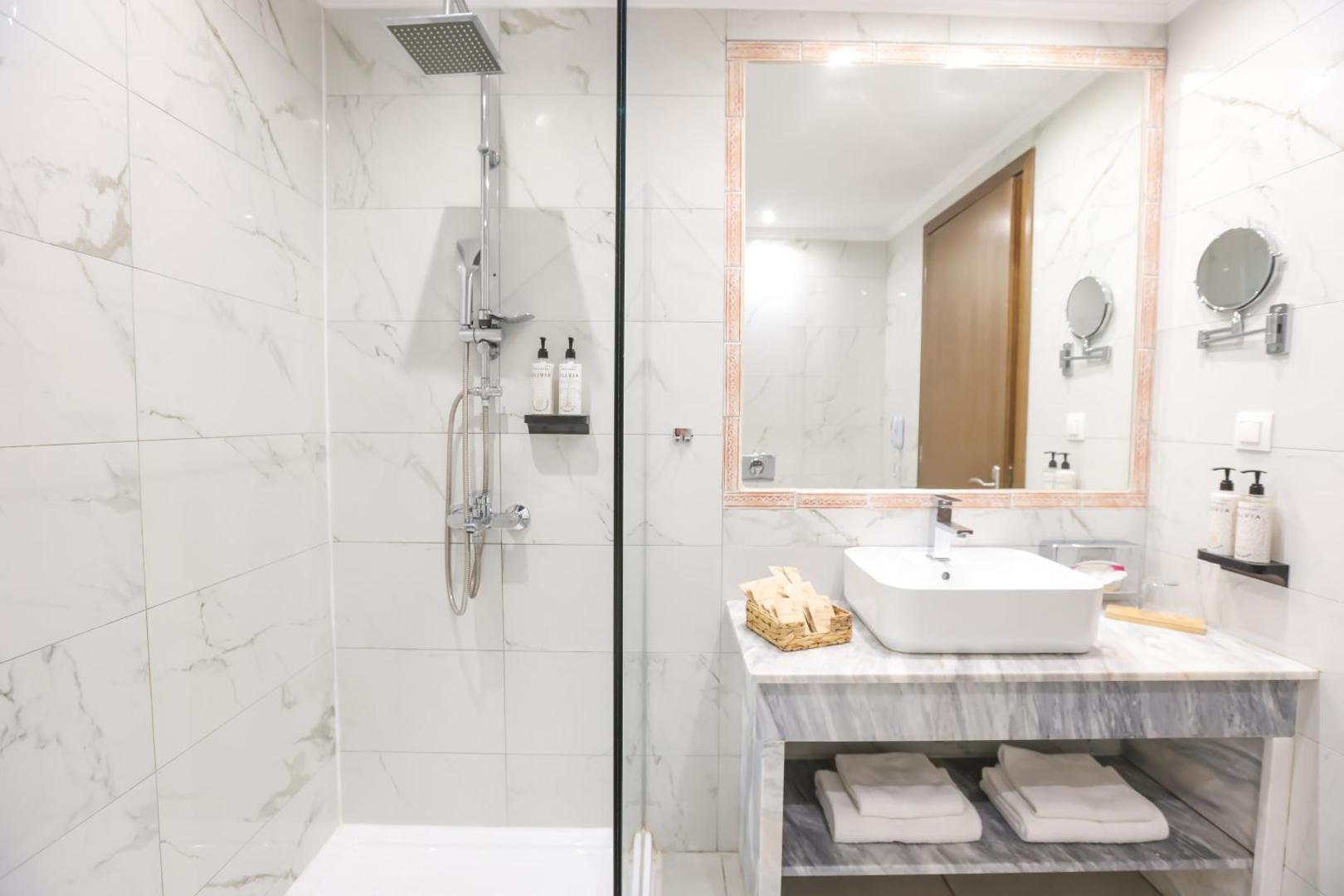 Mythos Palace Resort numura vannas istaba ar marmora apdari, plašu dušu un lielu spoguli — elegants dizains un komforts