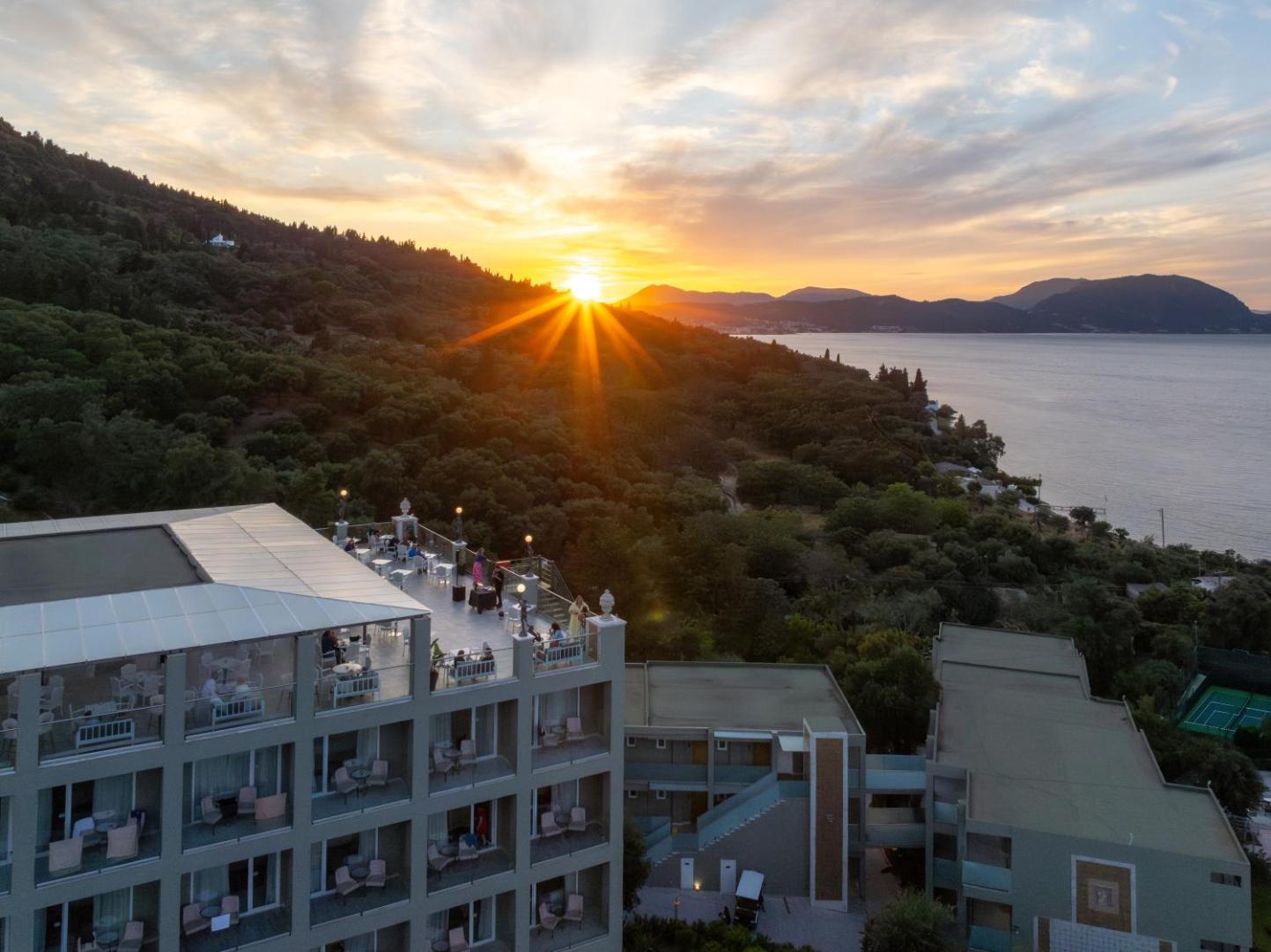 Mythos Palace Resort jumta terase saulrieta laikā Korfu salā — skats uz Jonijas jūru un apkārtējiem zaļajiem kalniem